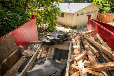 A large red dumpster filled with construction debris, including wood scraps and black roofing shingles.