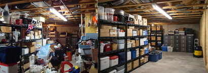 A cluttered storage basement with wooden ceiling beams, filled with metal shelves stocked with boxes and file cabinets.