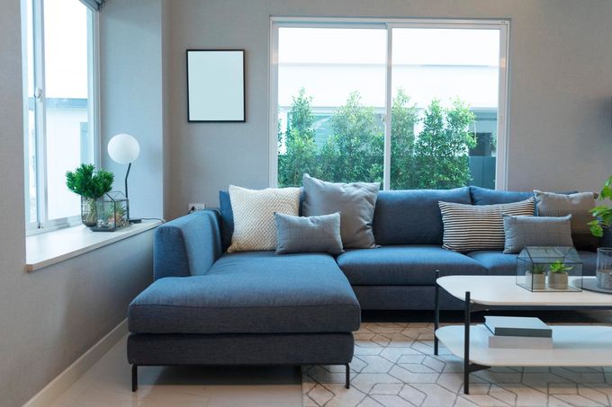 Un divano componibile blu con vari cuscini in un luminoso soggiorno moderno con ampie finestre e un tavolino da caffè in marmo.