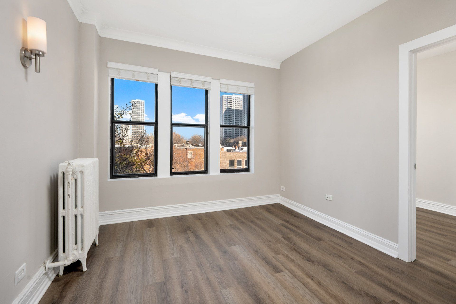An empty room with hardwood floors , two windows and a radiator at Reside on Clarendon.