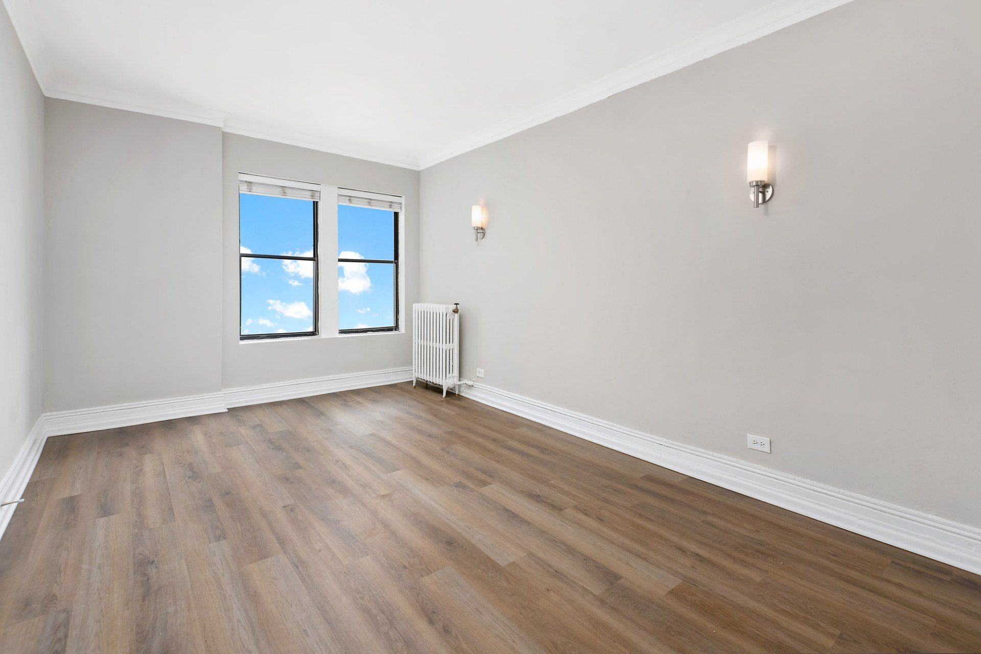 An empty room with hardwood floors and two windows at Reside on Clarendon.