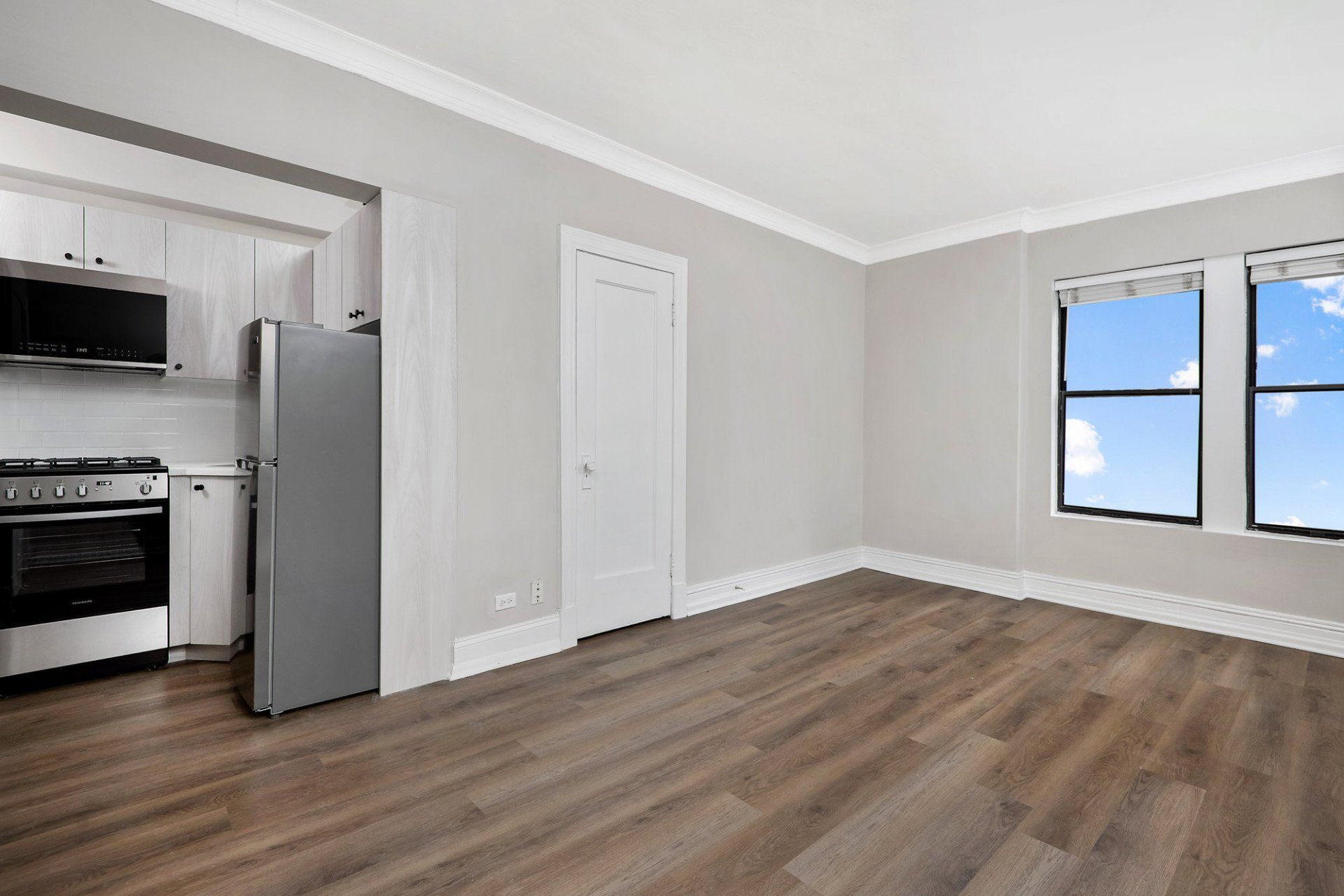 An empty living room with hardwood floors and a kitchen in the background at Reside on Clarendon.