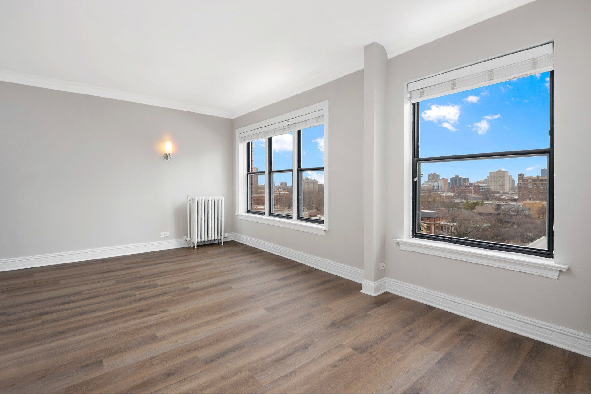 An empty living room with hardwood floors and two windows at Reside on Clarendon.