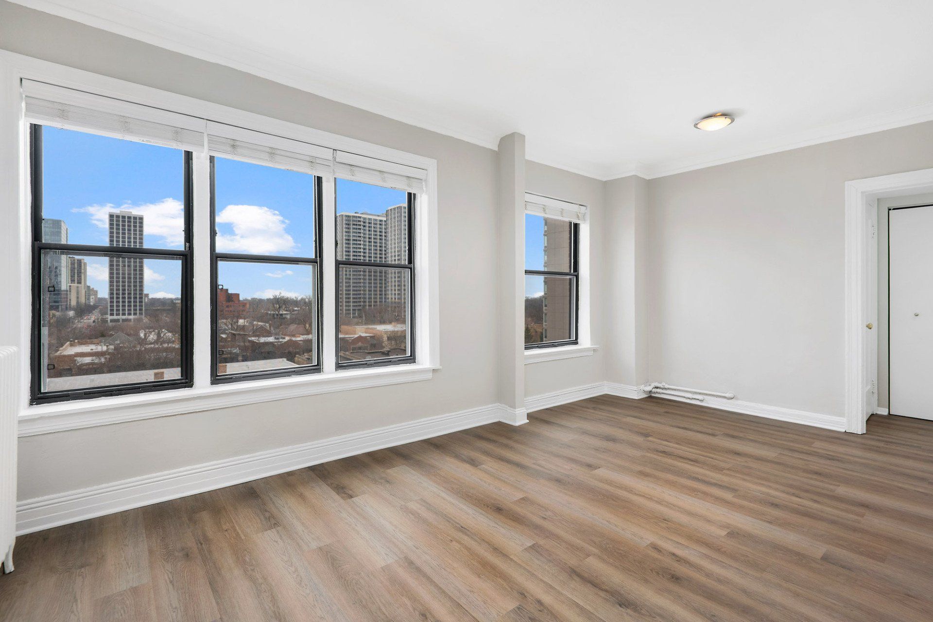 An empty living room with hardwood floors and two windows at Reside on Clarendon.