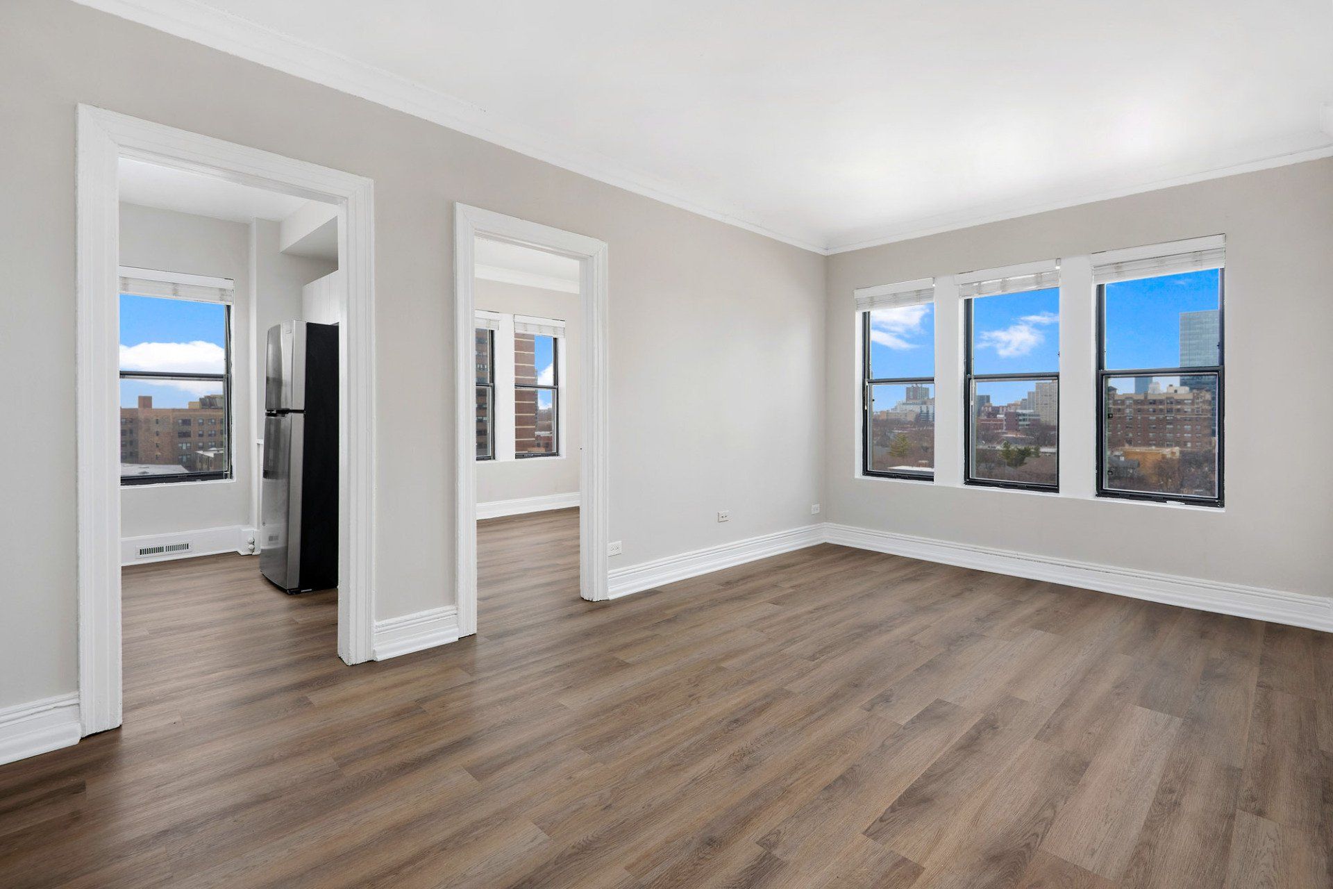 An empty living room with hardwood floors and a refrigerator at Reside on Clarendon.