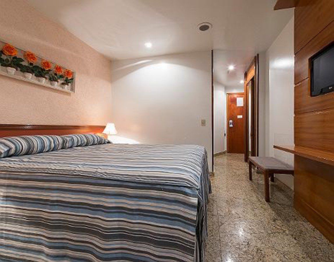 Um quarto de hotel com uma cama, televisão e banco.