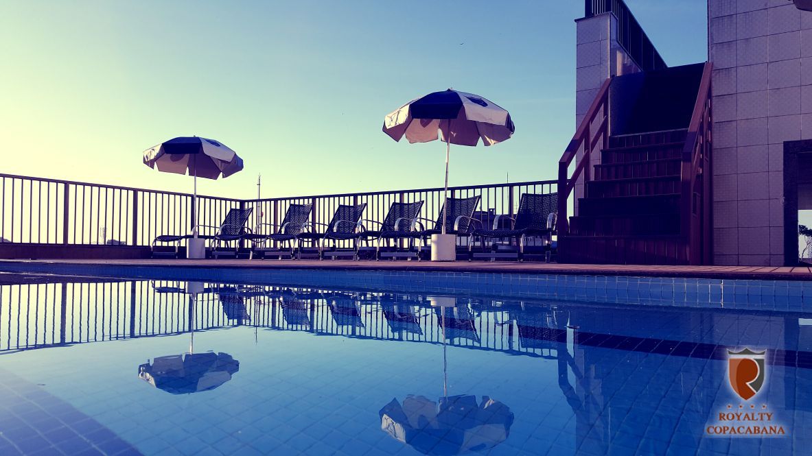 Uma piscina com guarda-sóis e cadeiras ao fundo