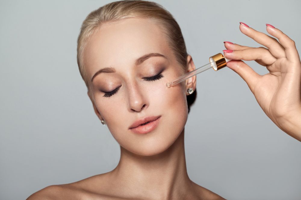 A Woman is Applying a Serum to Her Face With a Pipette — Kàllos Aesthetics by Nurse Kellie In Maryborough, QLD