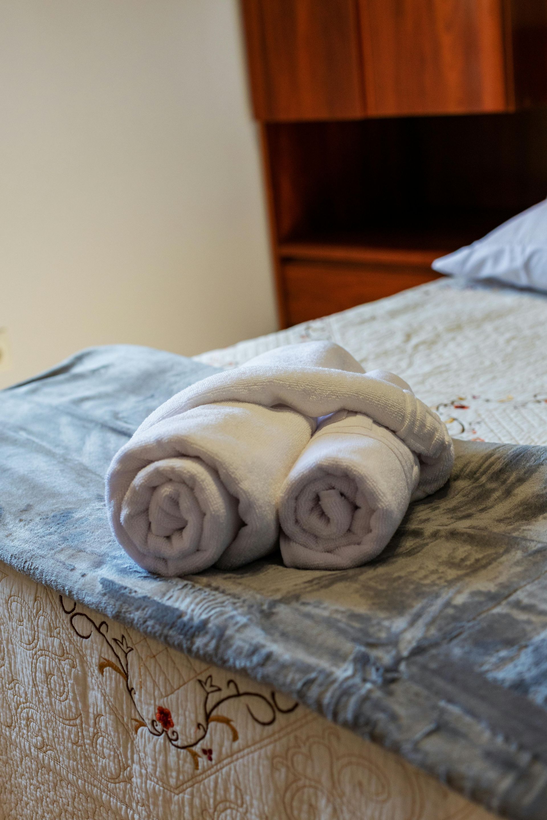 Rolled white towels arranged on a gray blanket on a bed.