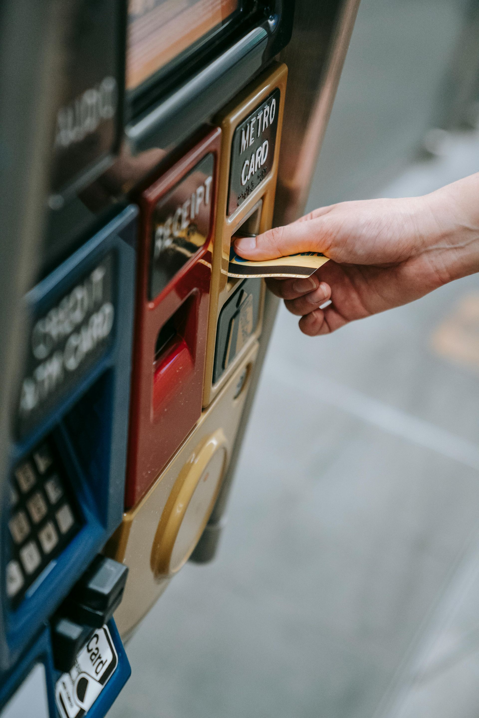 Person inserting a card into a ticket machine slot. The machine has slots for receipts and other cards.