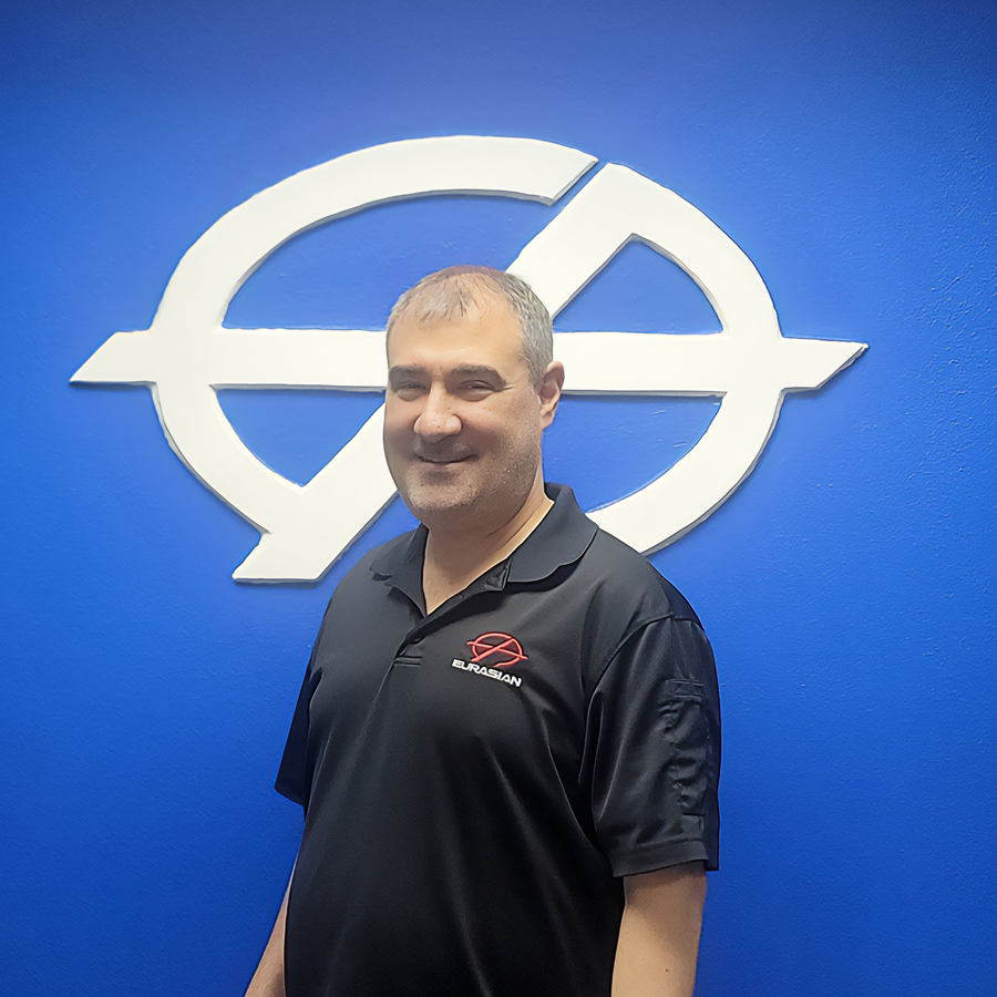 Man in black shirt smiles in front of a blue wall with a white logo.
