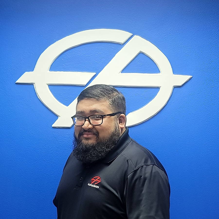 Man with glasses and beard in black shirt smiling in front of a blue wall with a white logo.