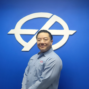 Man in blue shirt smiles in front of a blue wall with a white logo.