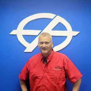 Man in red shirt stands in front of a blue wall with a white logo.