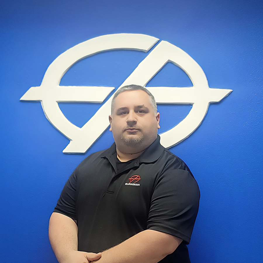 Man in black polo shirt stands in front of a blue wall with a white logo.