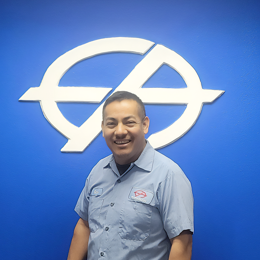 Man in blue uniform smiles in front of a blue wall with a white logo.