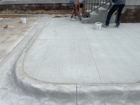 Two men are working on a concrete sidewalk next to stairs.