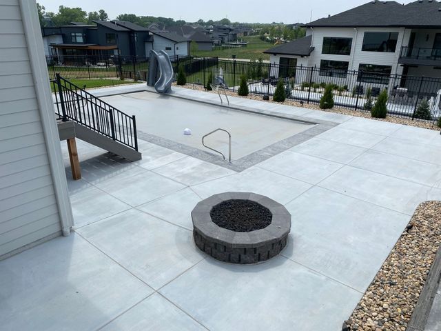 A fire pit is in the middle of a patio next to a pool.