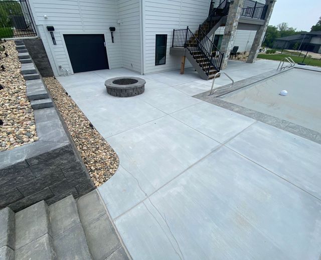 A concrete patio with a fire pit and stairs next to a house.