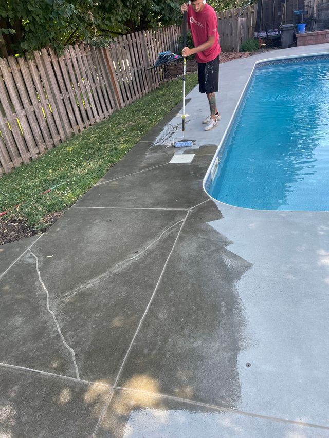 A man is mopping the sidewalk next to a swimming pool.