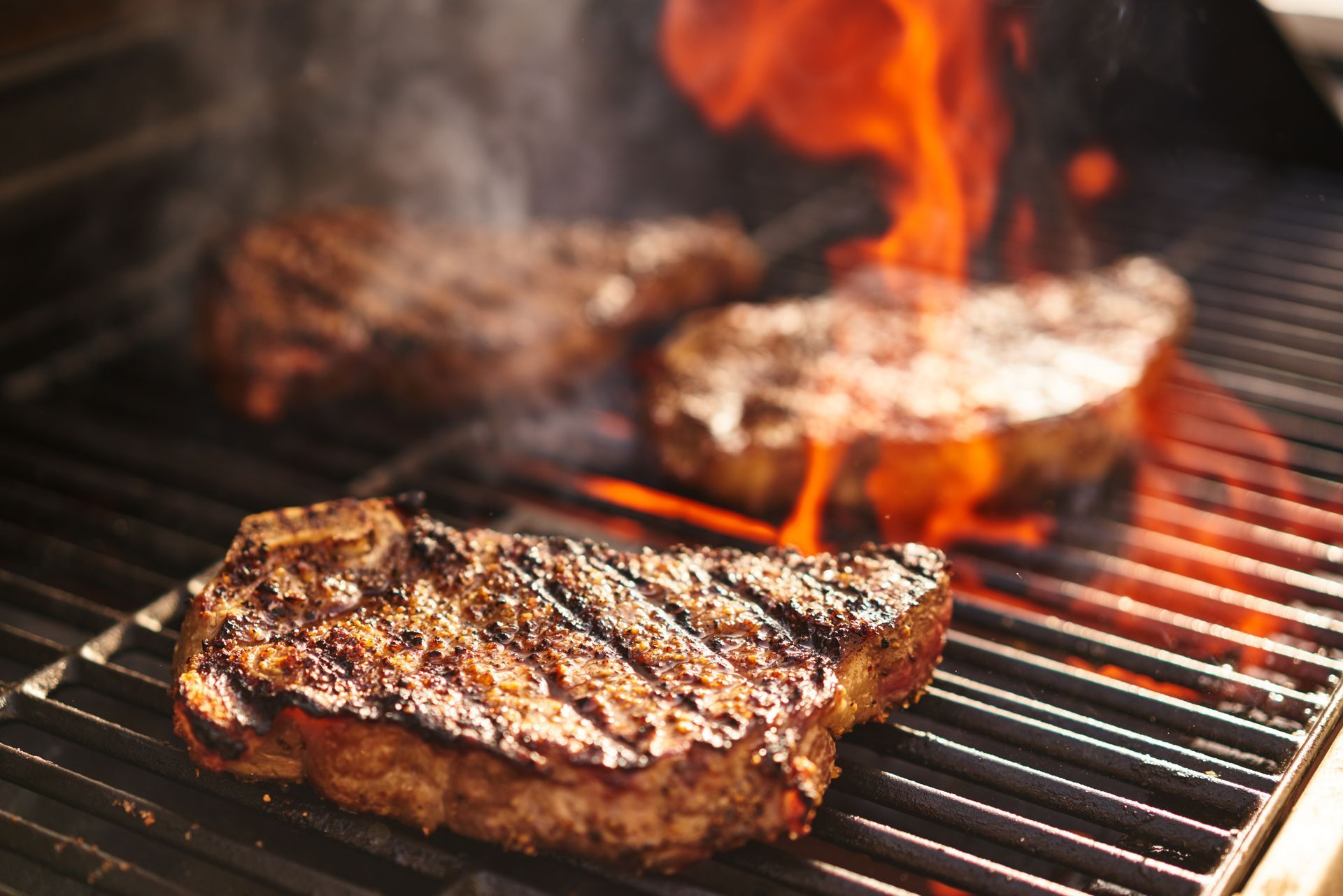 Two steaks are cooking on a grill with flames coming out of them.