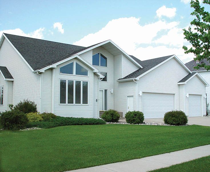 A white house with a black roof and white garage doors