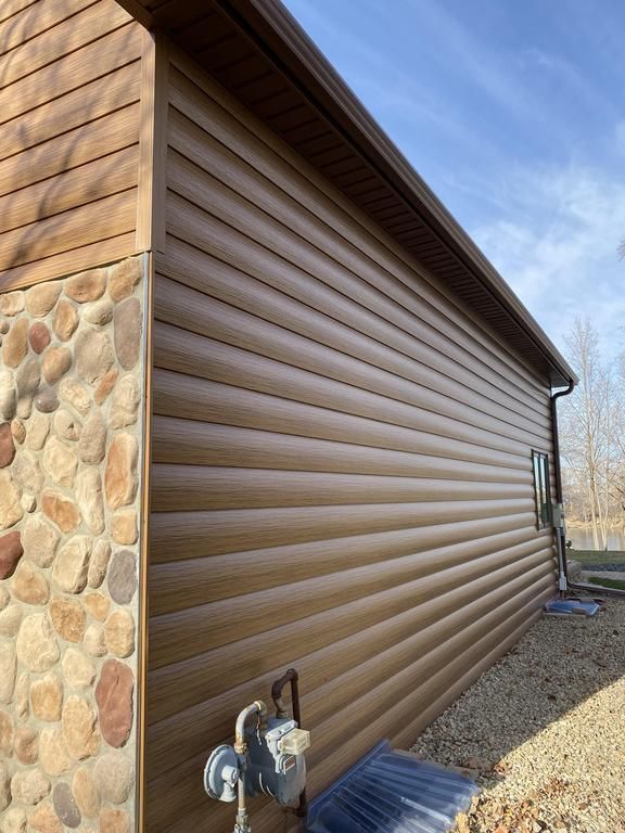 The side of a house with log siding and a stone wall.