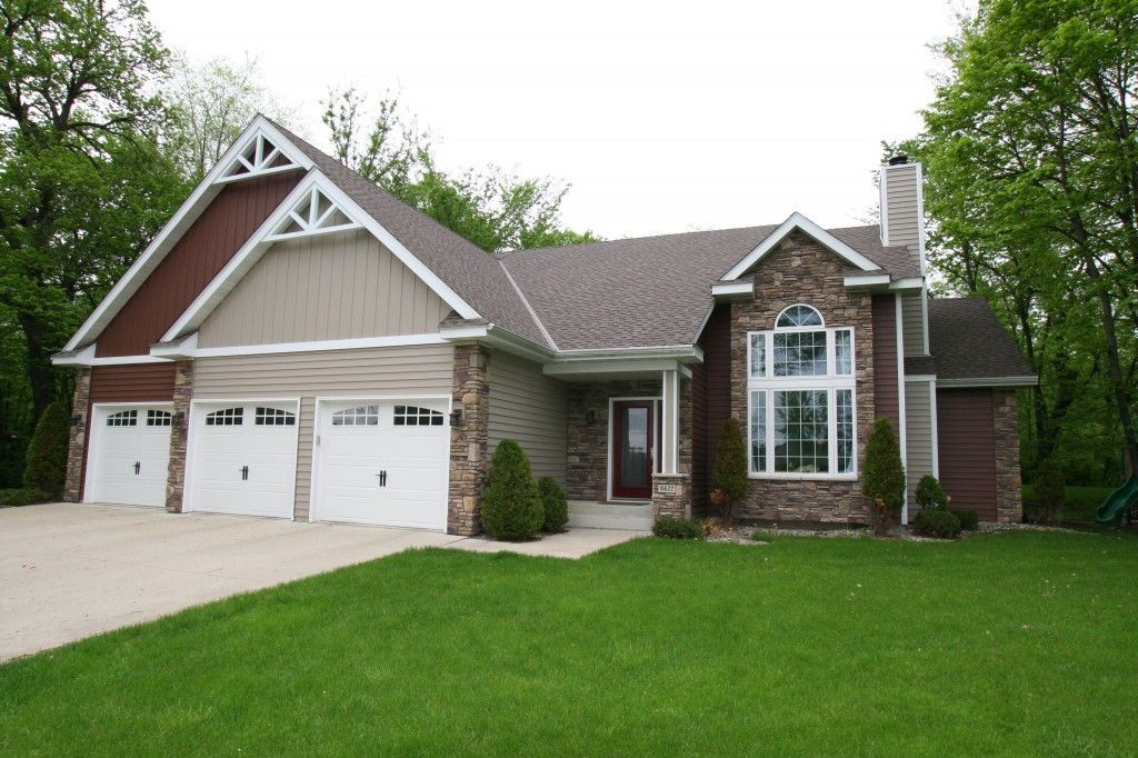 A large house with three garage doors and a large lawn in front of it.