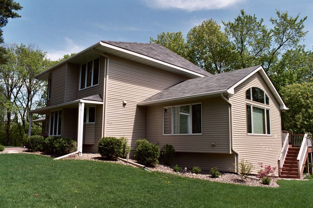 A large house with a lot of windows sits on a lush green hillside