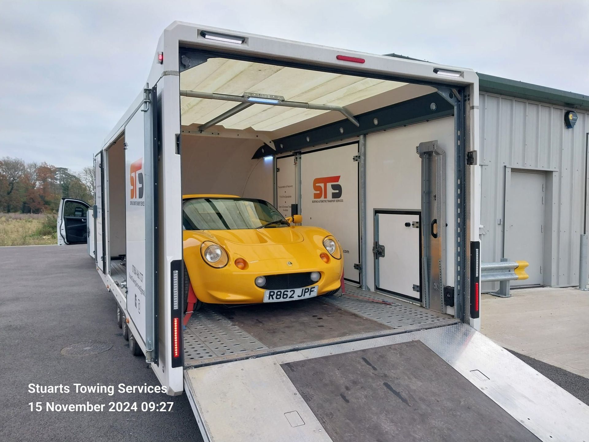 Yellow sports car loaded in a white enclosed car transport trailer.