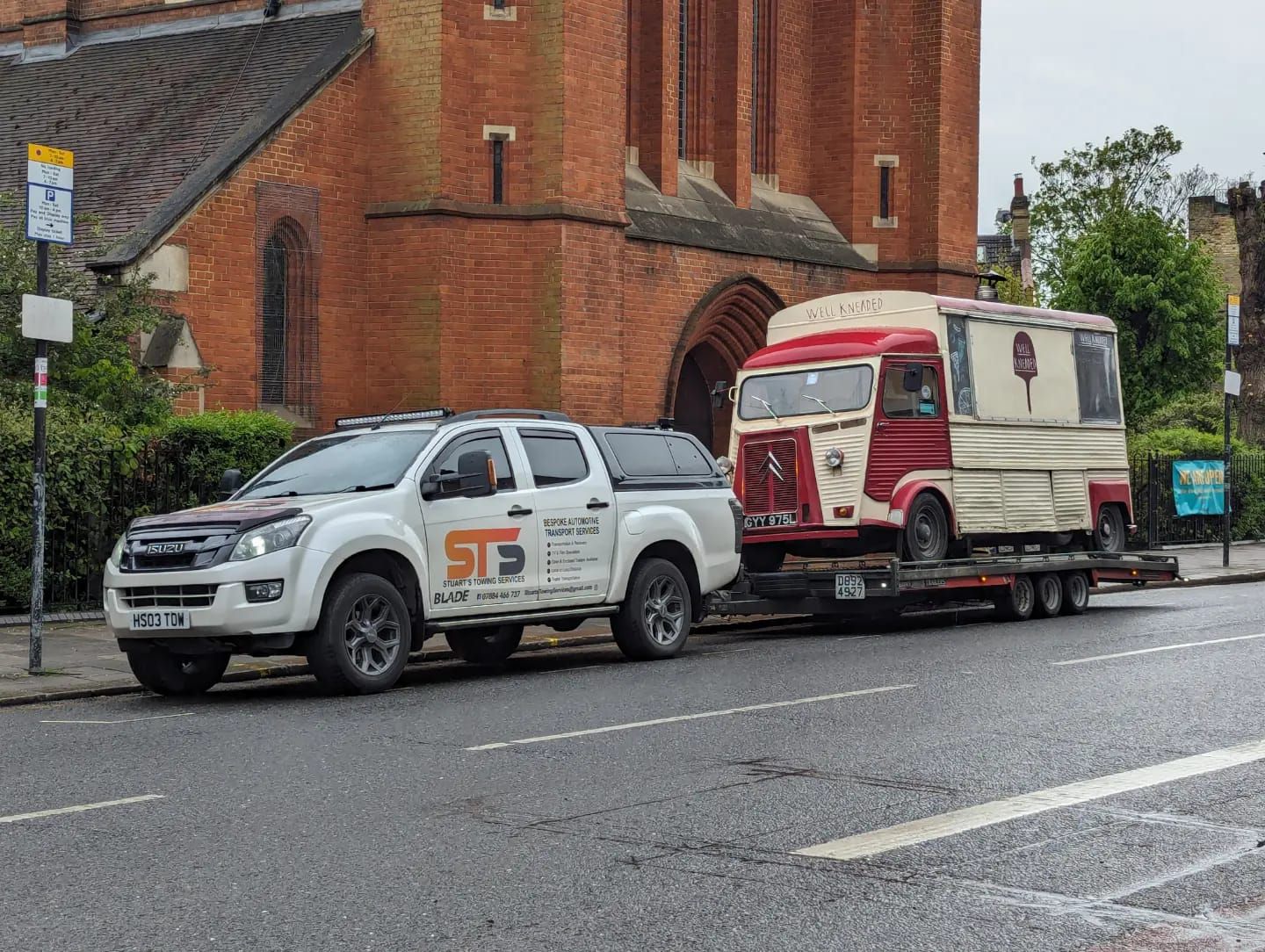 White truck towing a vintage red and white trailer in front of a brick church.