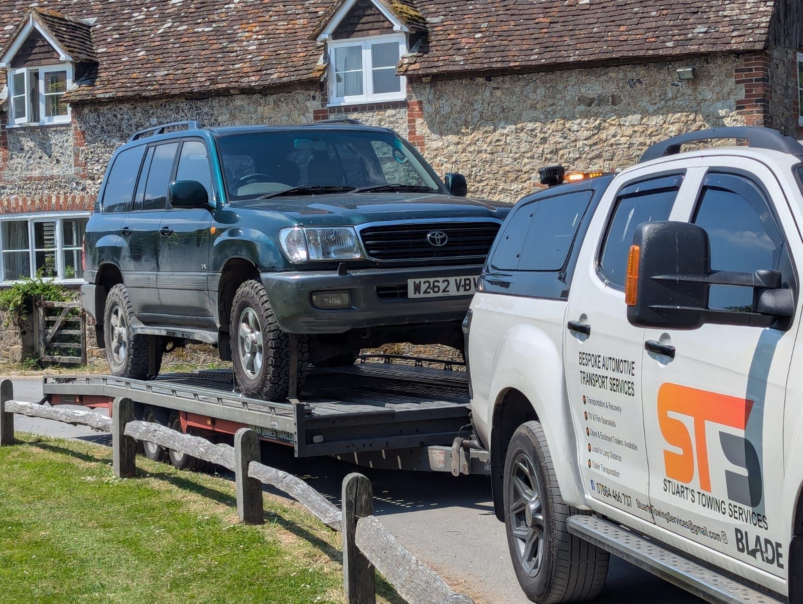 A green SUV being towed by a white tow truck on a sunny day in front of a building.