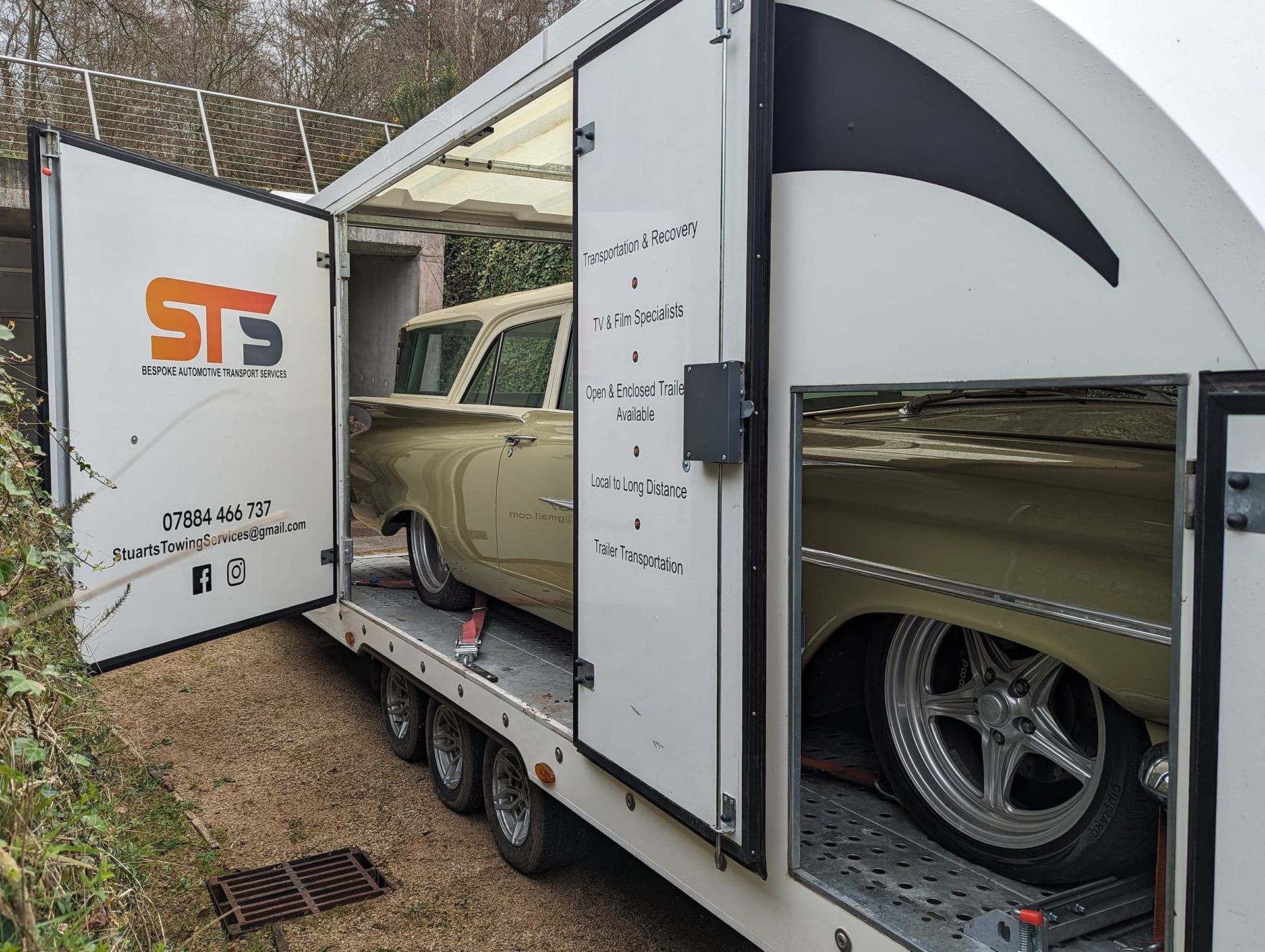 A vintage beige car loaded in a white transport trailer with open doors.