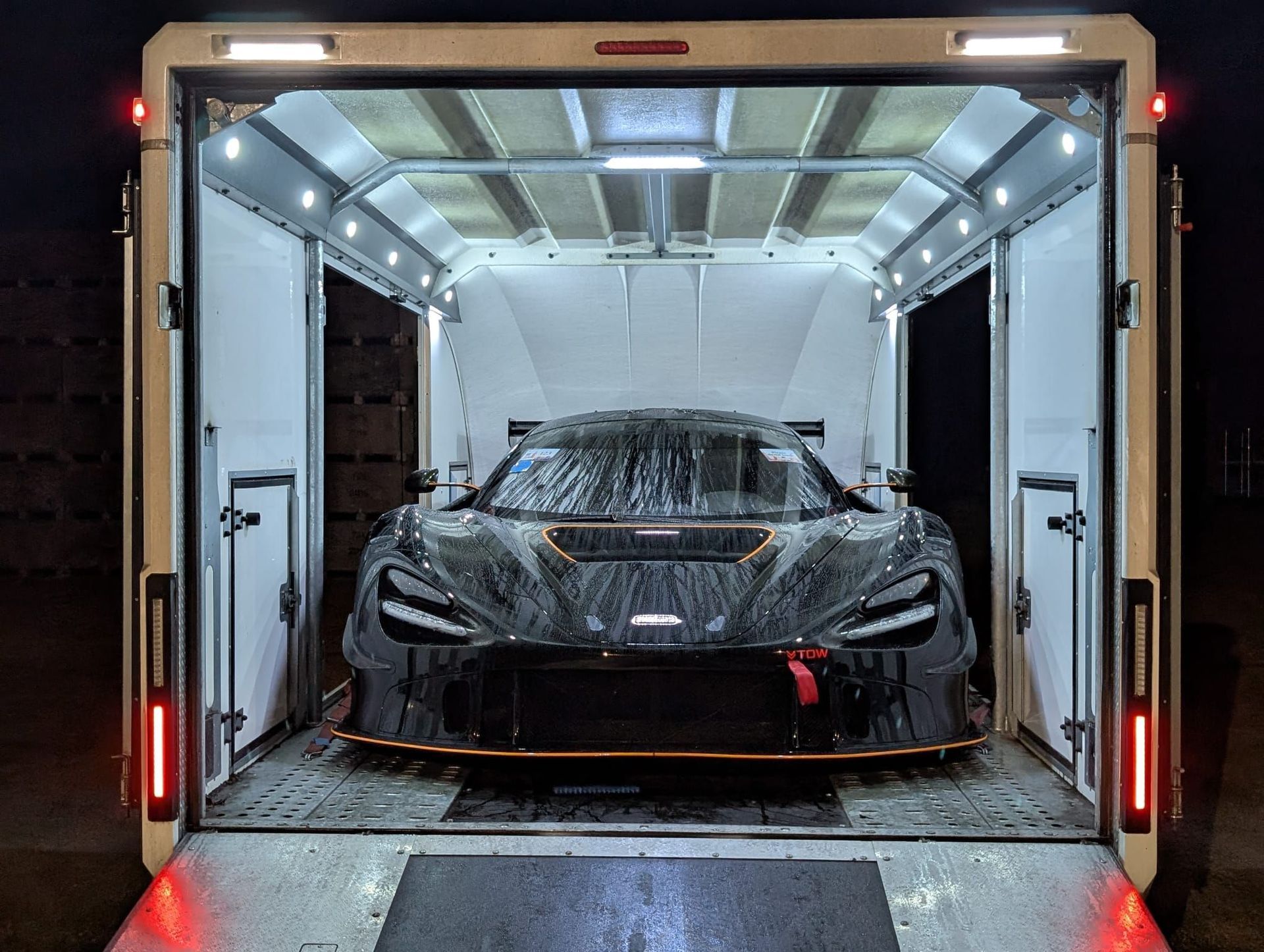 A black McLaren race car sits inside an illuminated white trailer.