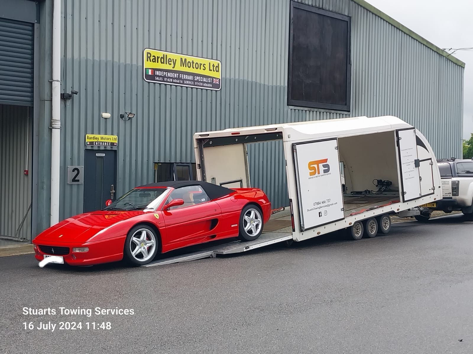 Red Ferrari convertible being loaded into a white enclosed car trailer outside a building.