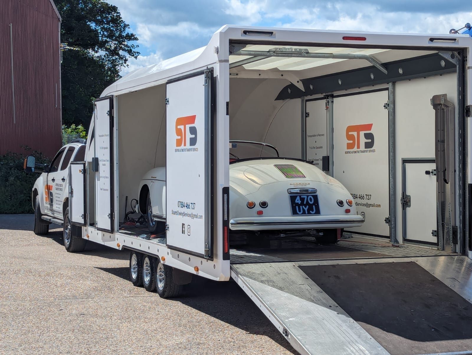 White Porsche 356 being loaded into a white enclosed car trailer. Trailer and truck have company logos.