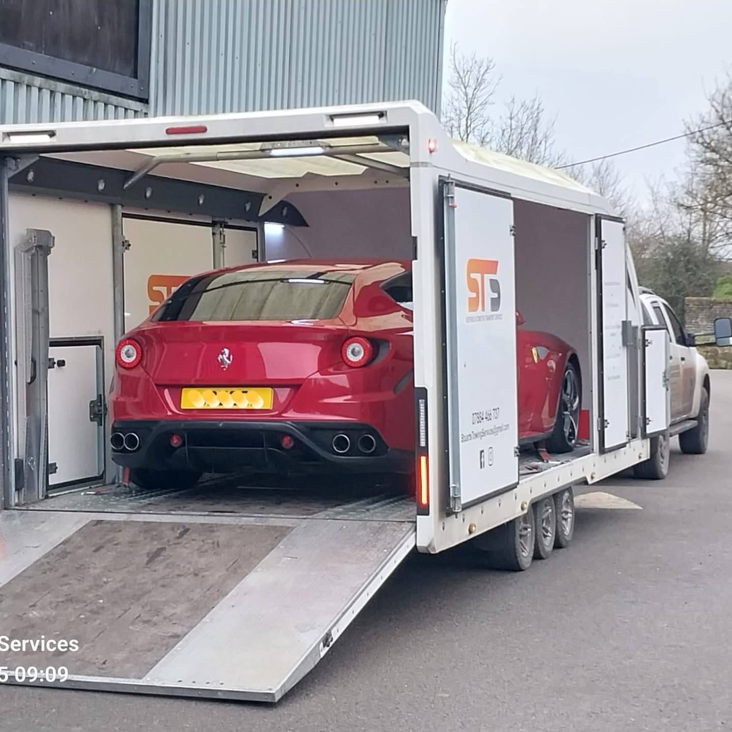 Red Ferrari being transported in a white enclosed trailer, pulled by a pickup truck.