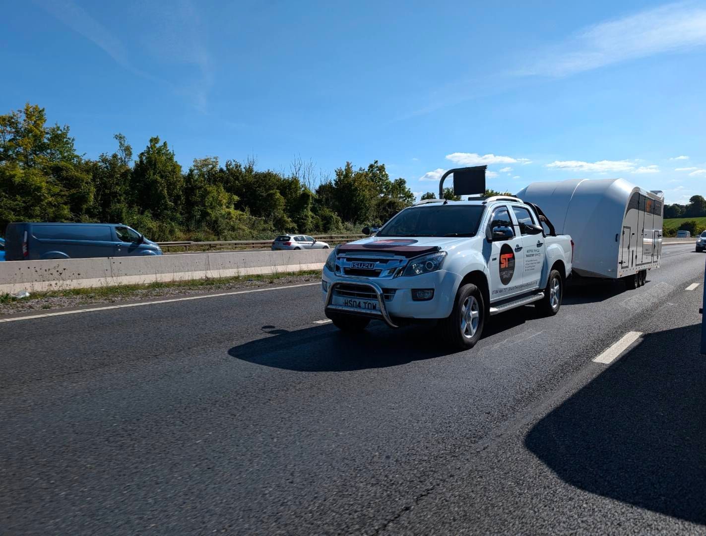 White pickup truck towing a caravan on a highway, sunny day.