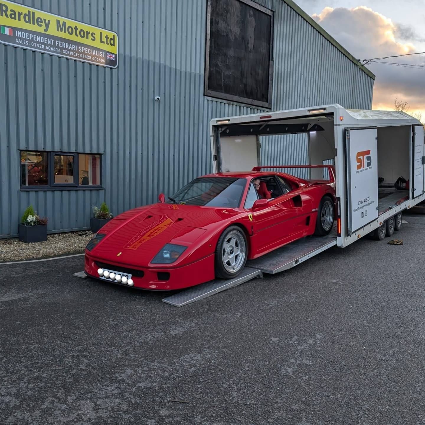 Red Ferrari F40 being loaded onto a white car transport trailer outside a business.
