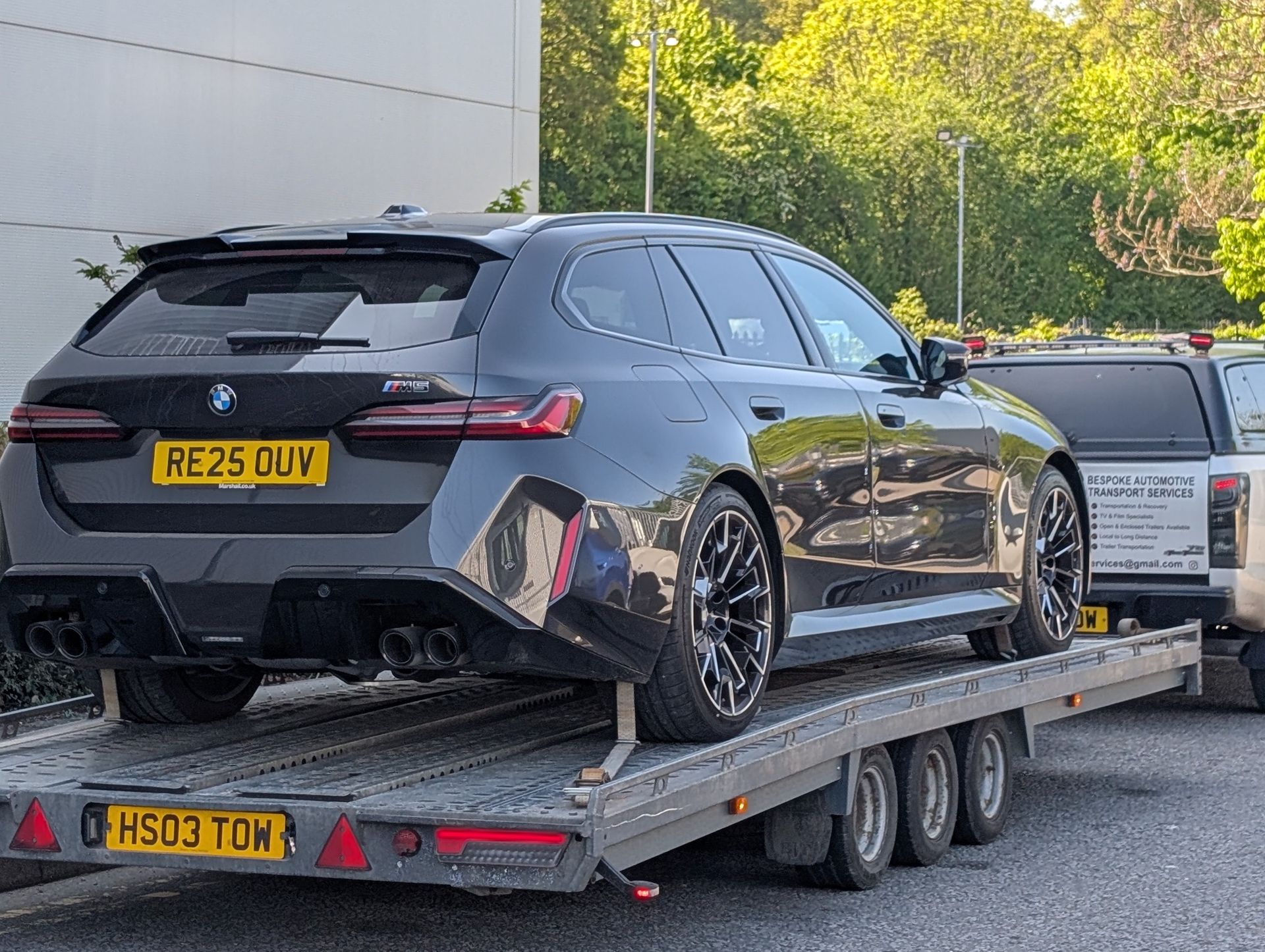 A black BMW M5 Touring station wagon on a trailer. Rear view, license plate visible.