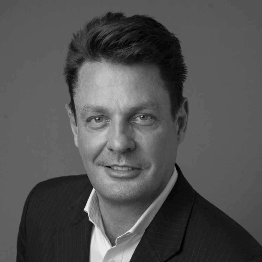 A man in a suit and white shirt is smiling in a black and white photo.