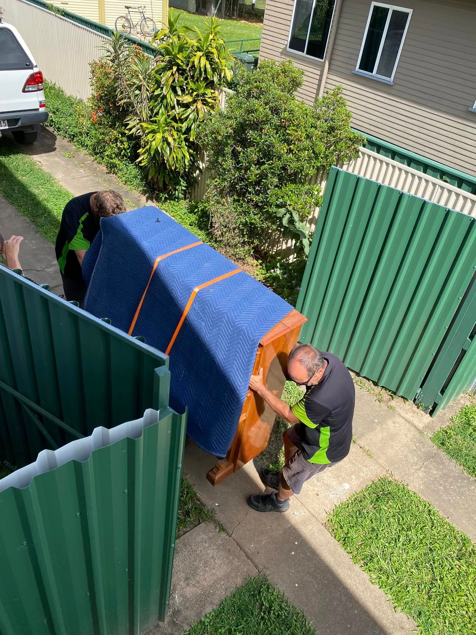 Two Movers Carry a Blue-covered Piano Down a Walkway — Little Green Truck Bundaberg In Gin Gin, QLD