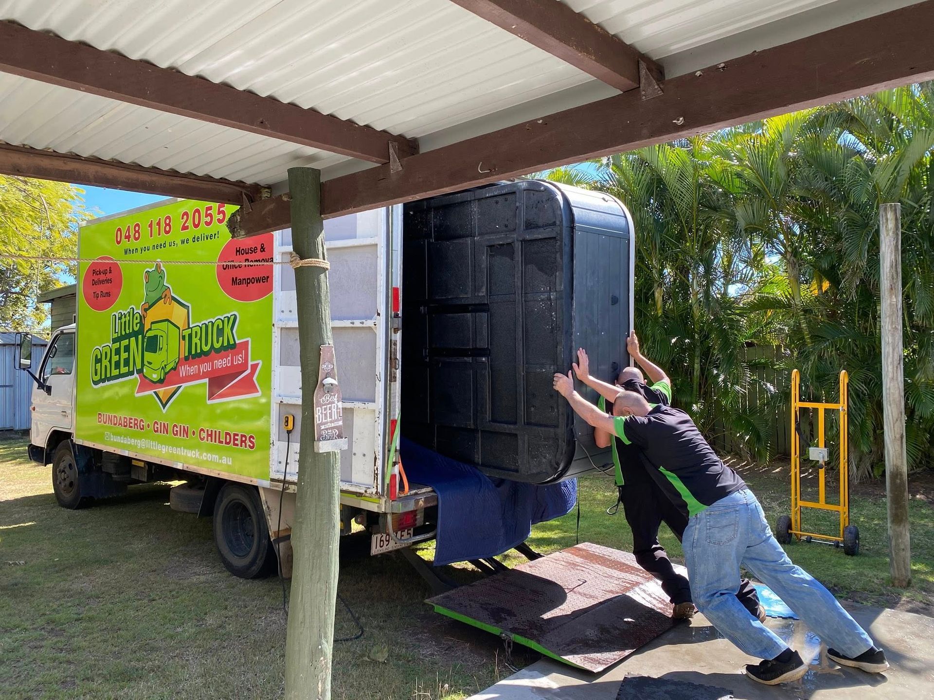 Two Men Pushing a Large Black Object Onto a Truck — Little Green Truck Bundaberg In Bundaberg, QLD