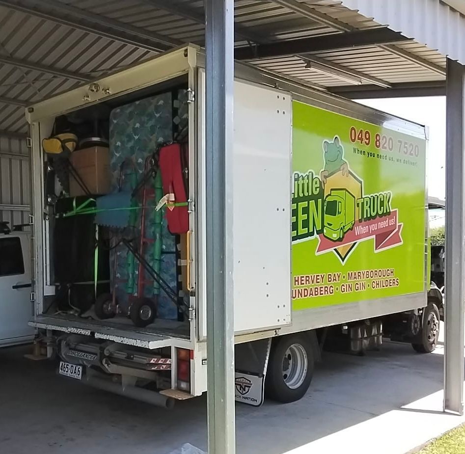 Moving truck loaded with items parked under a carport; green logo reads 