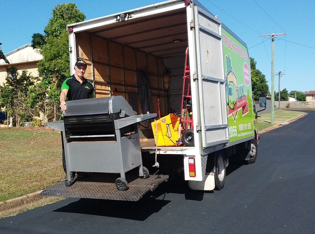 Man unloading a gray grill from a white moving truck on a sunny street. — Little Green Truck Bundaberg In Gin Gin, QLD