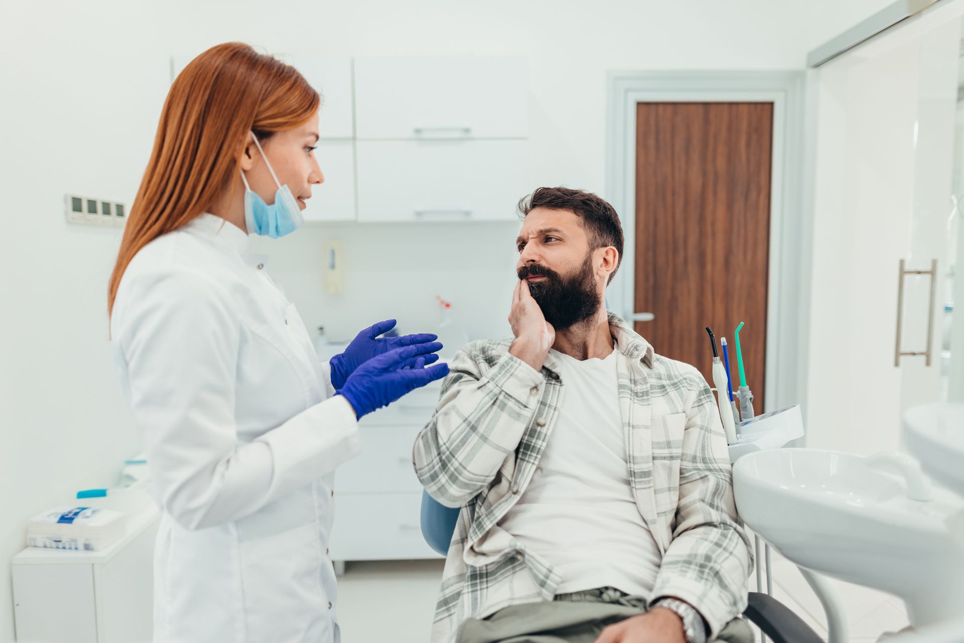 Dentist wearing face mask talking to patient with toothache in dental office Dentist wearing face mask talking to patient with toothache in dental office