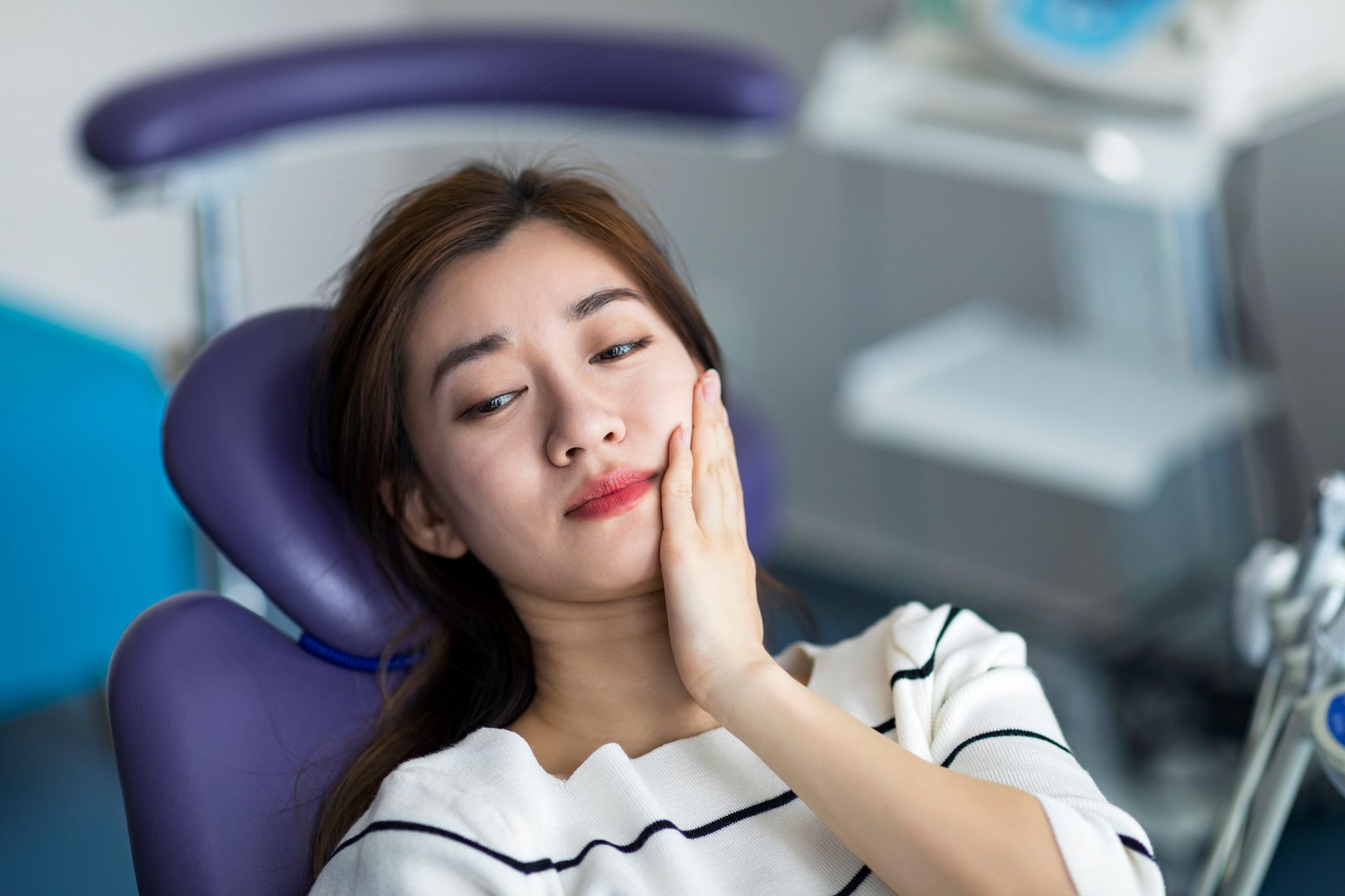 Young woman holding cheek in chair at dentist, having toothache