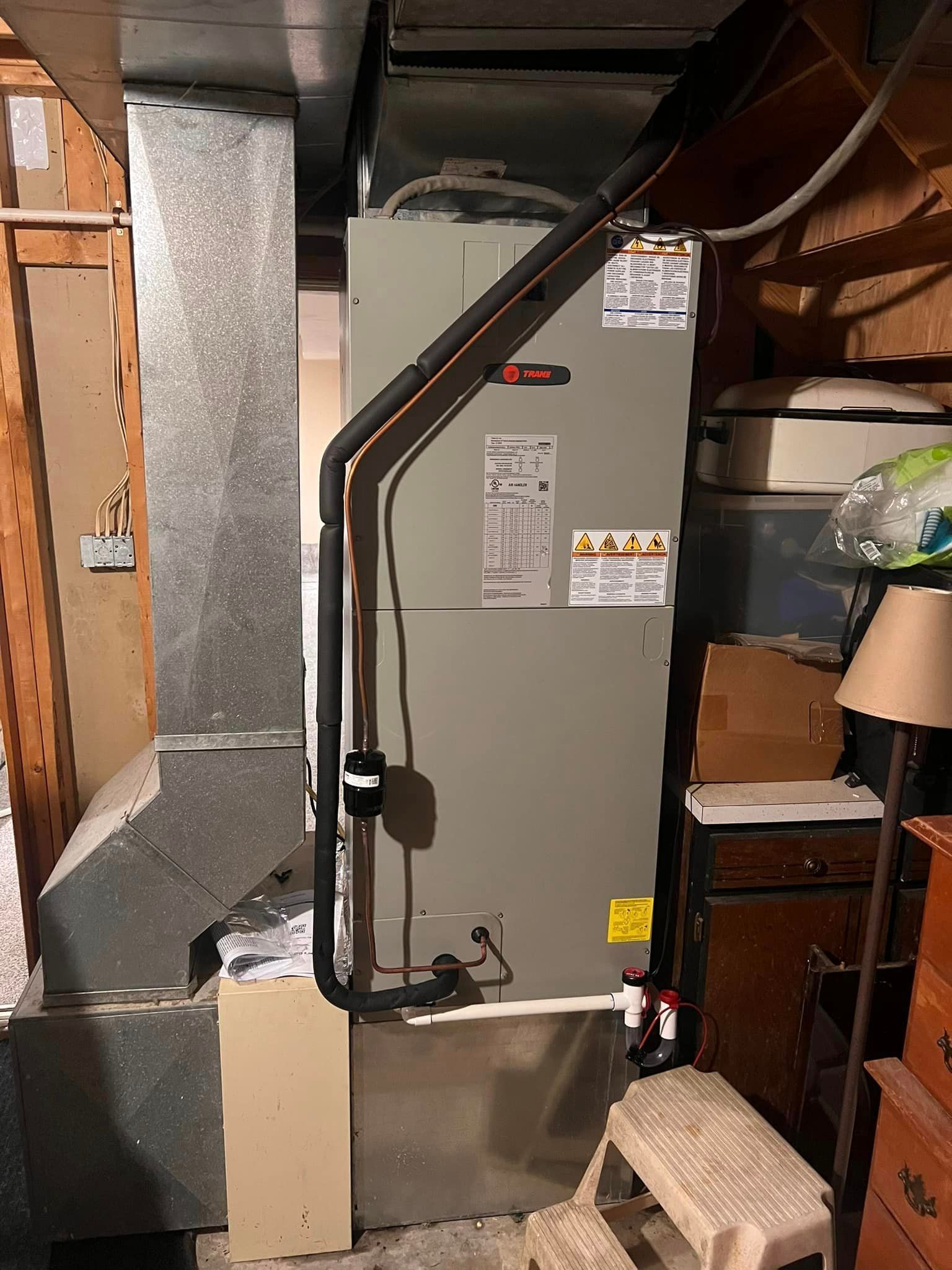 An air conditioner is sitting in a basement next to a staircase.