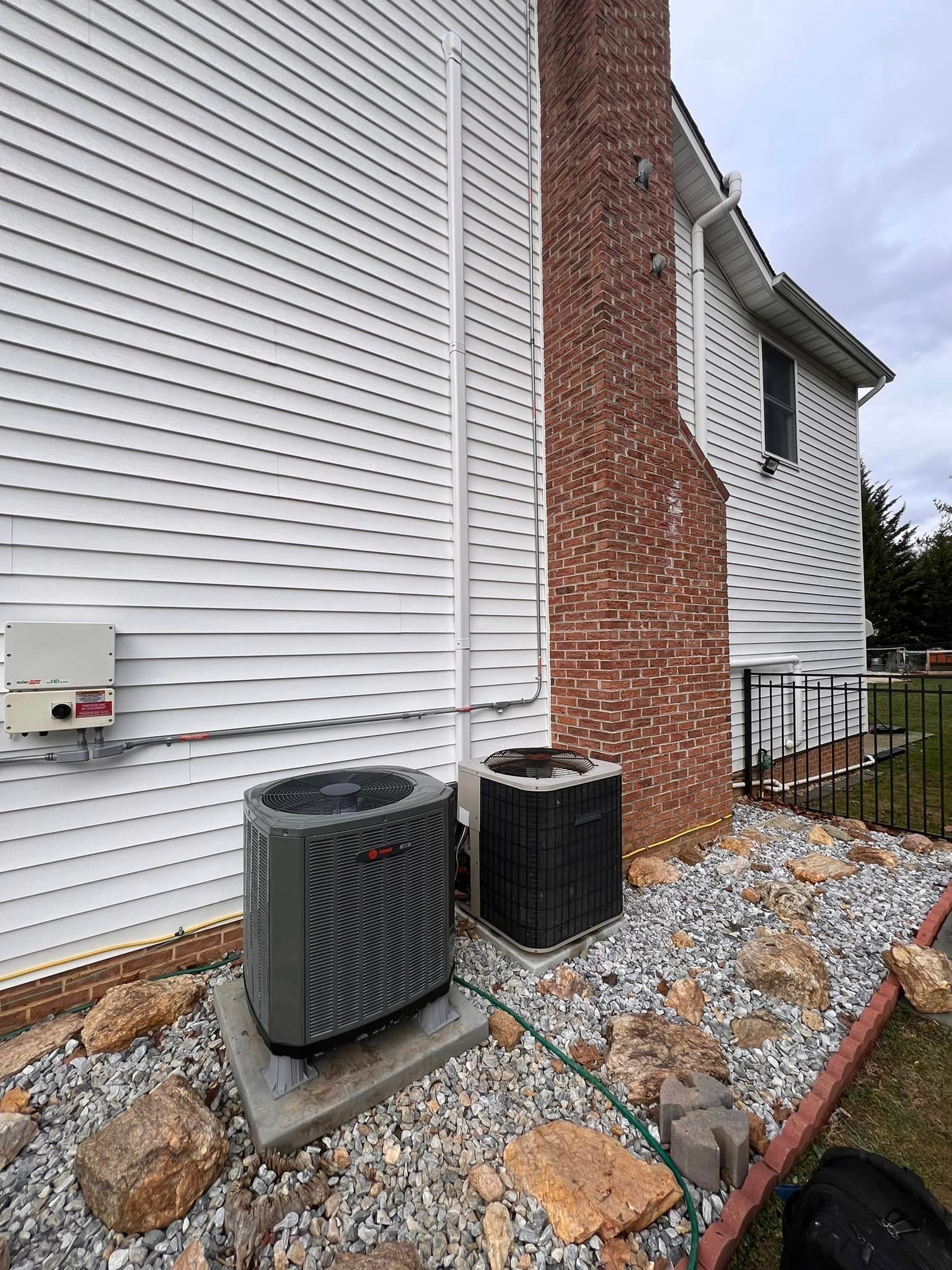 Two air conditioners are sitting on the side of a house.