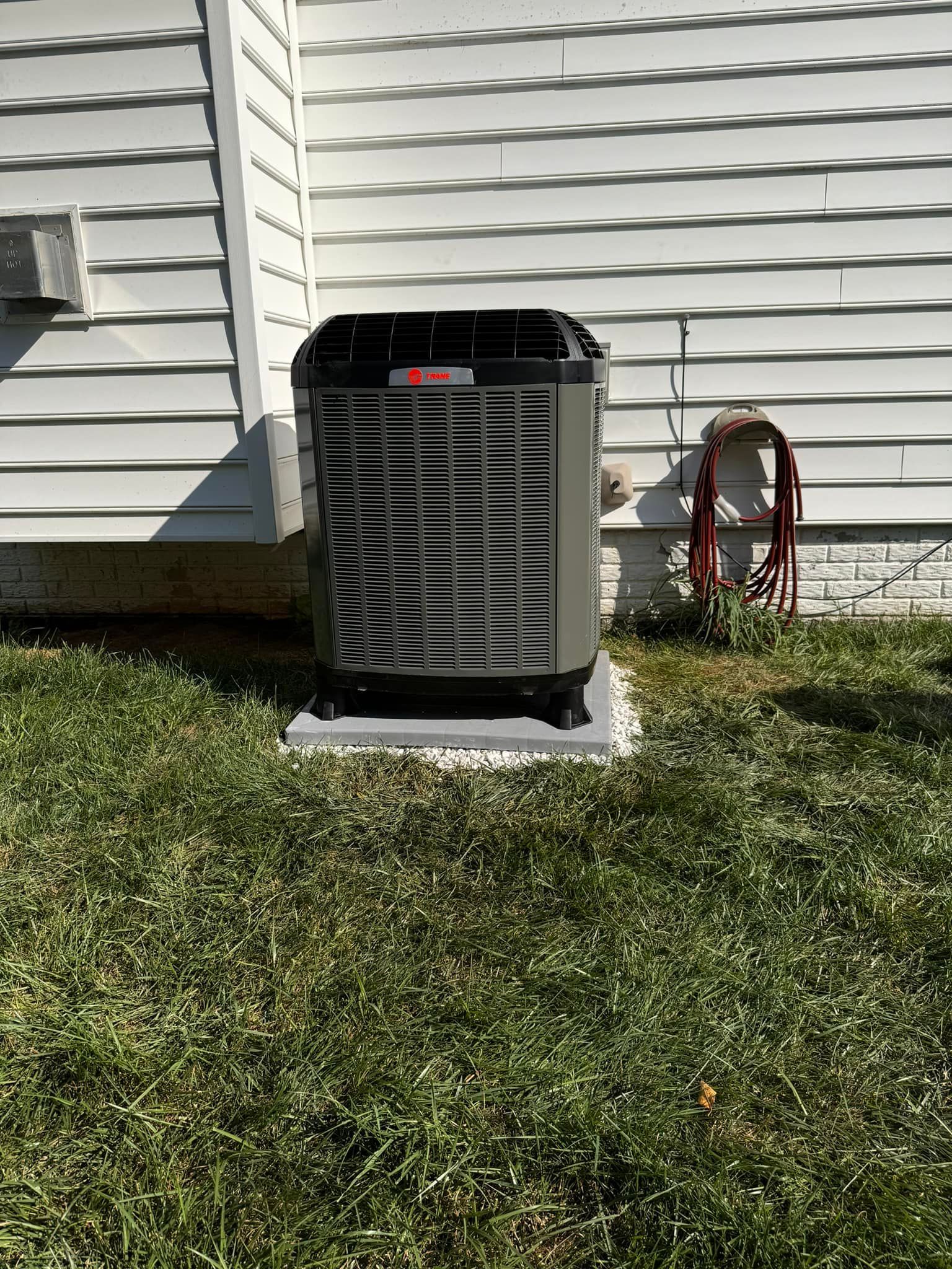 An air conditioner is sitting in the grass next to a house.